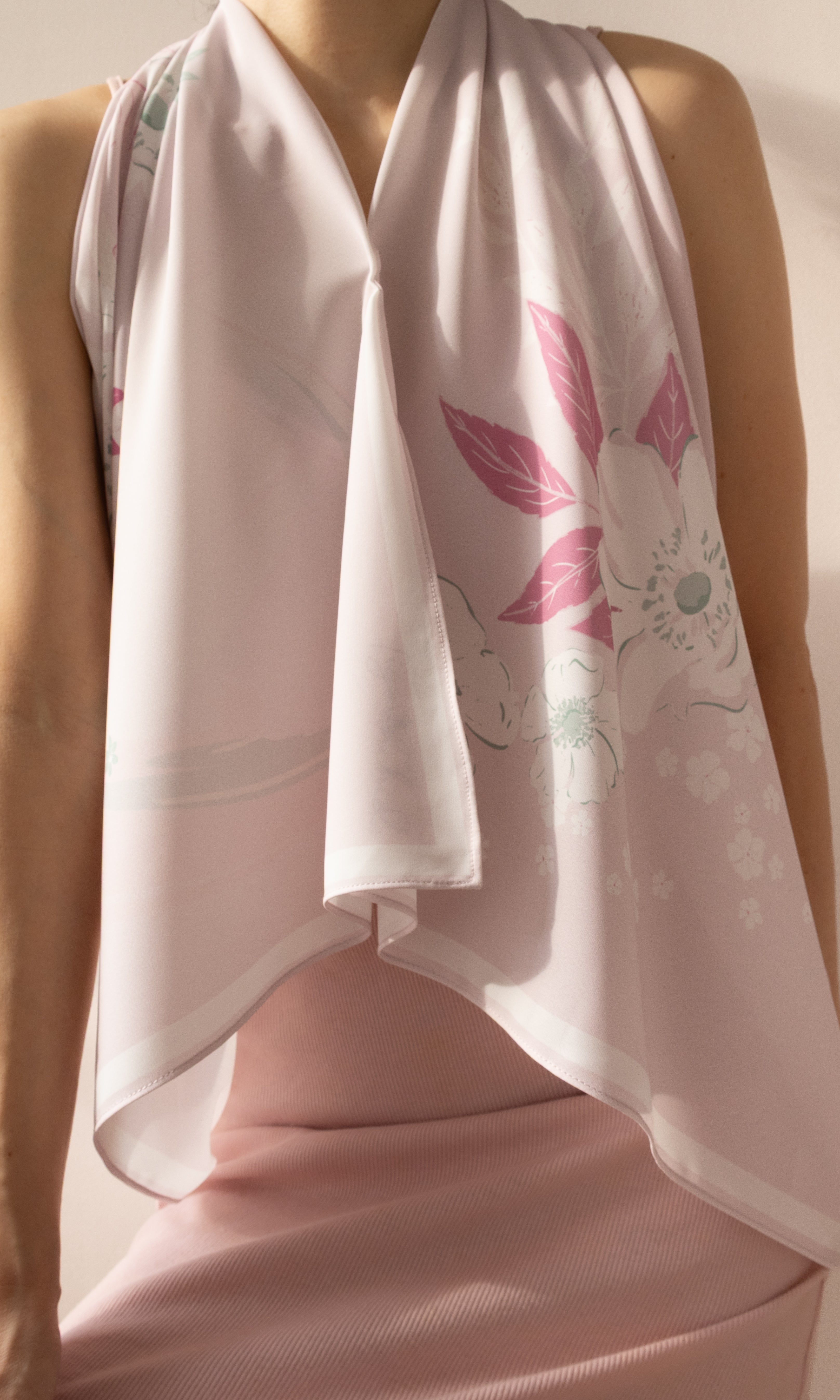 A close-up of a model wearing a light pink halter top and a matching draped scarf with a pink floral print.