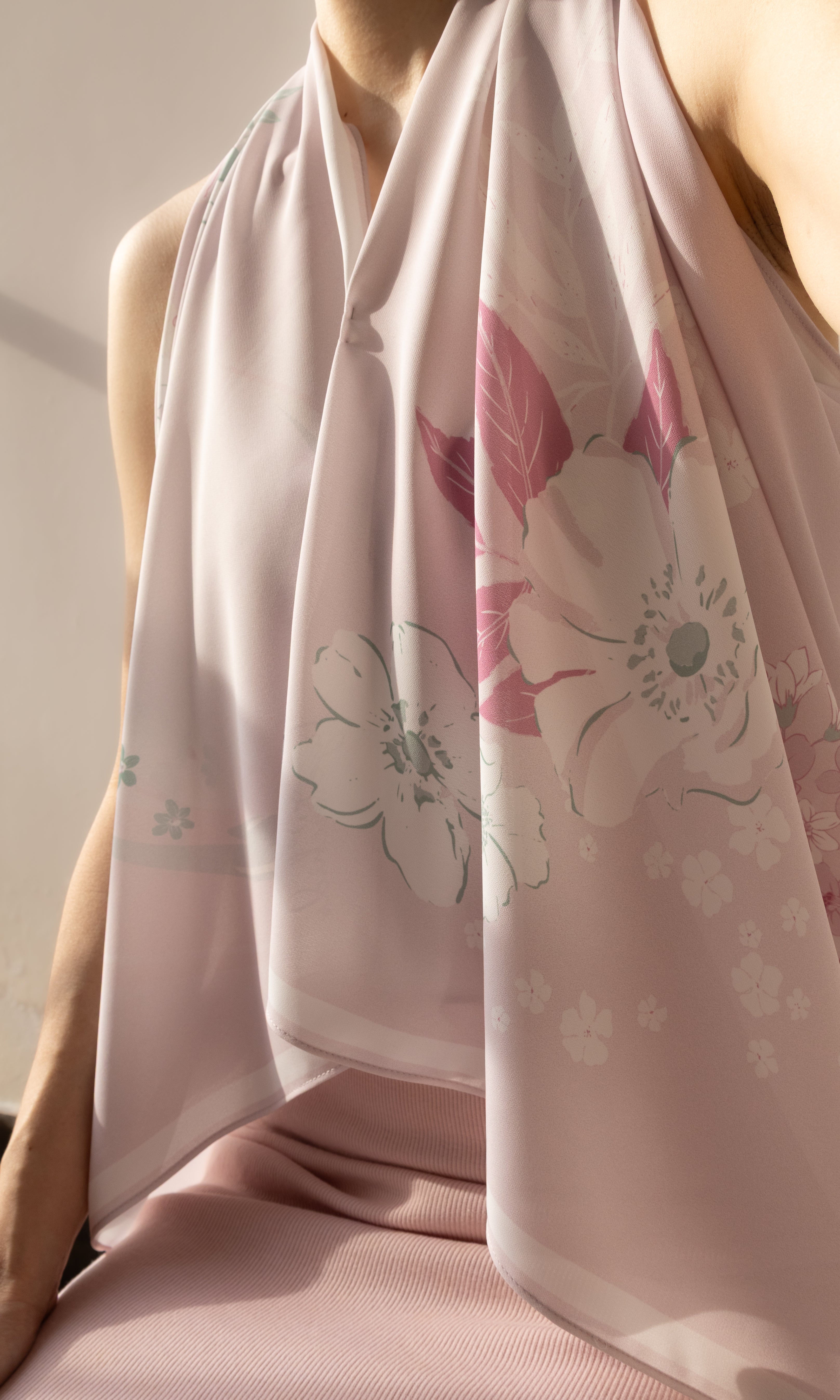 A close-up of a model wearing a light pink halter-neck top and a matching sheer pink scarf with a white and pink floral print.