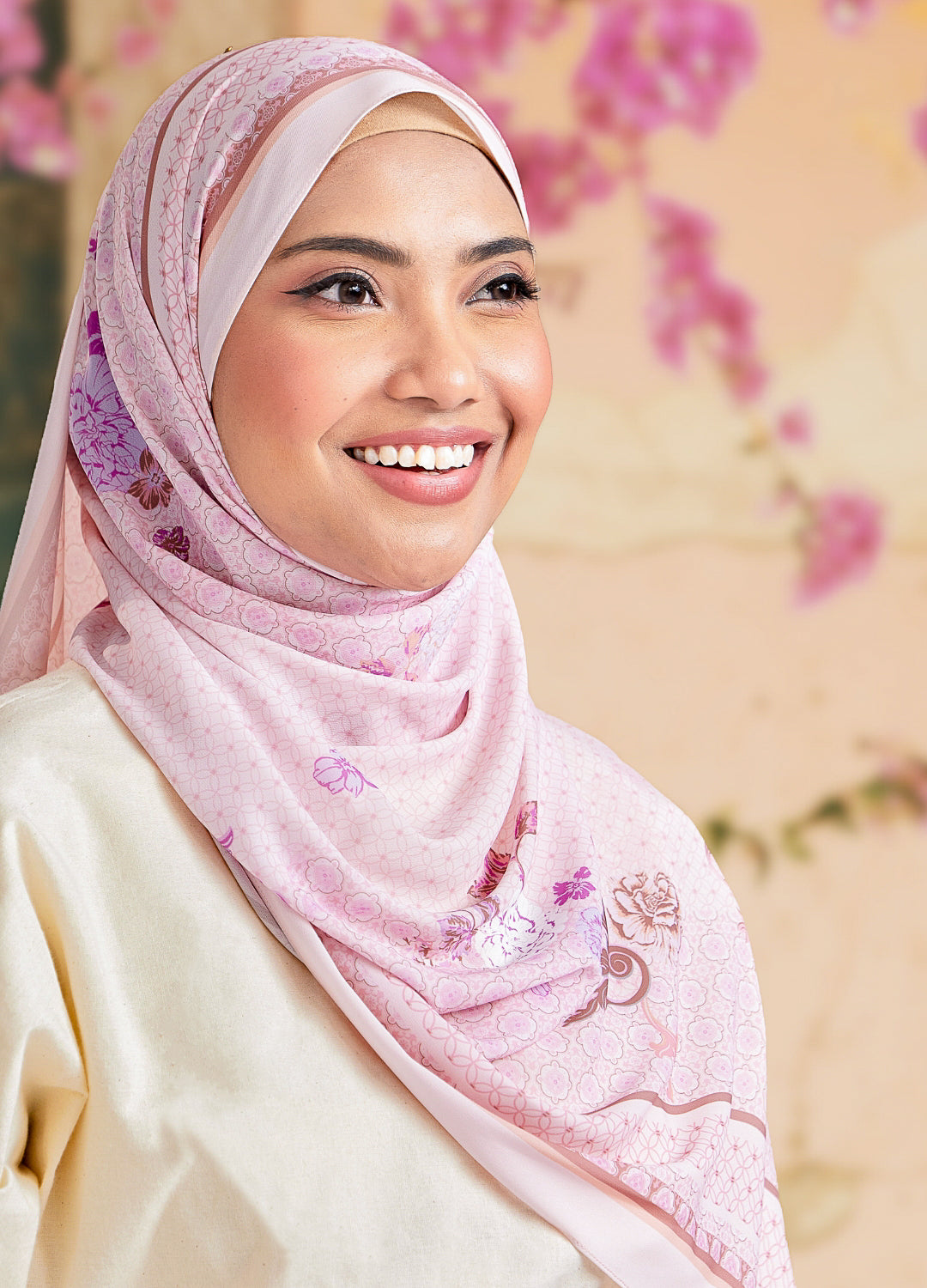 Woman wearing a pink hijab with floral patterns against a blurred floral background