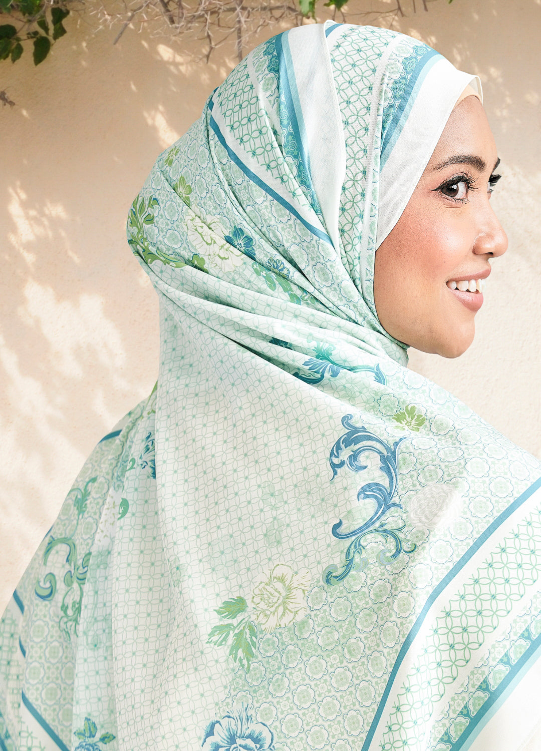 Woman wearing a light green hijab with floral patterns against a neutral background