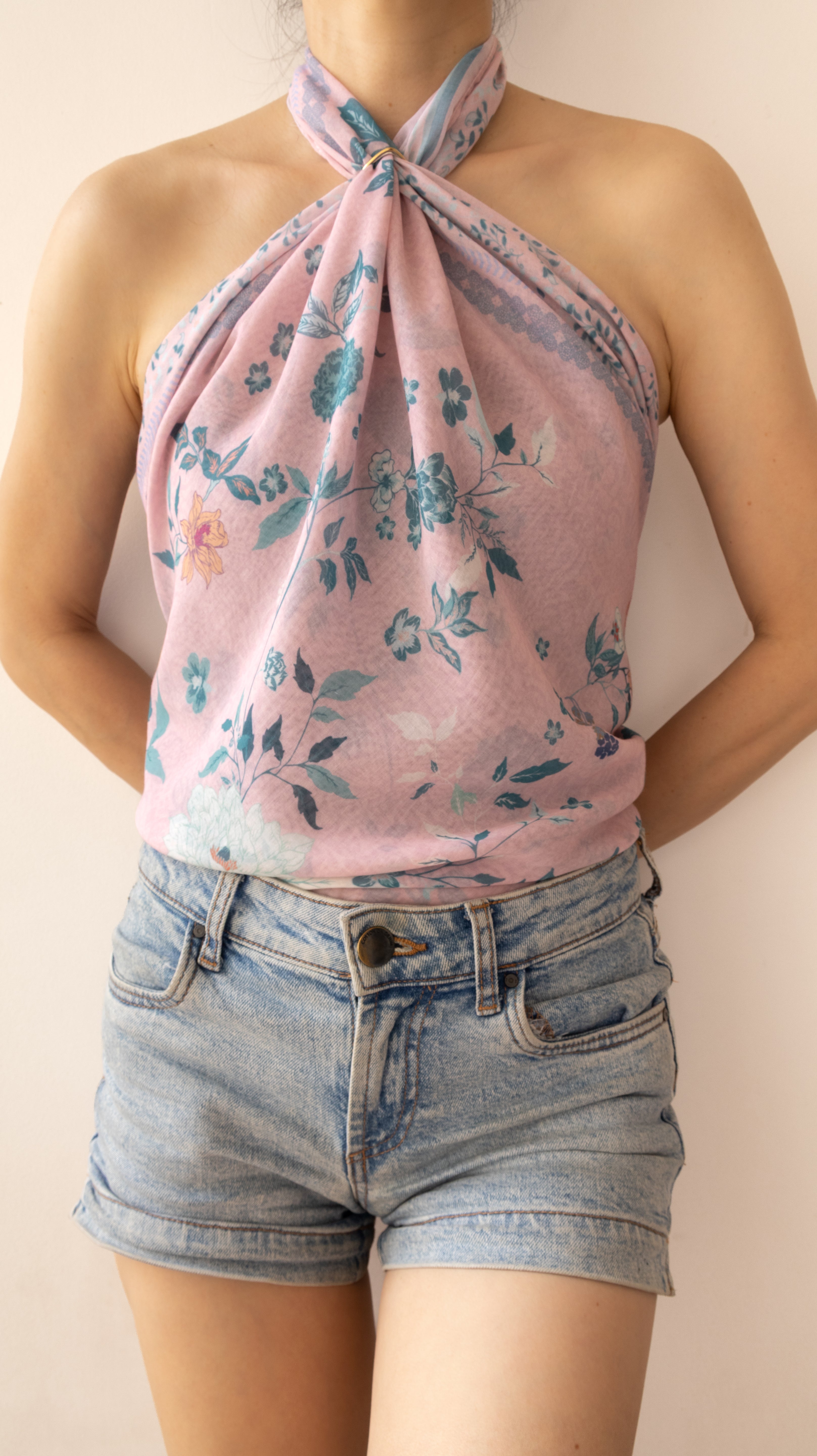 A woman wearing a light pink halter top with a blue and green floral print, paired with light-wash denim shorts, shown against a plain beige background.