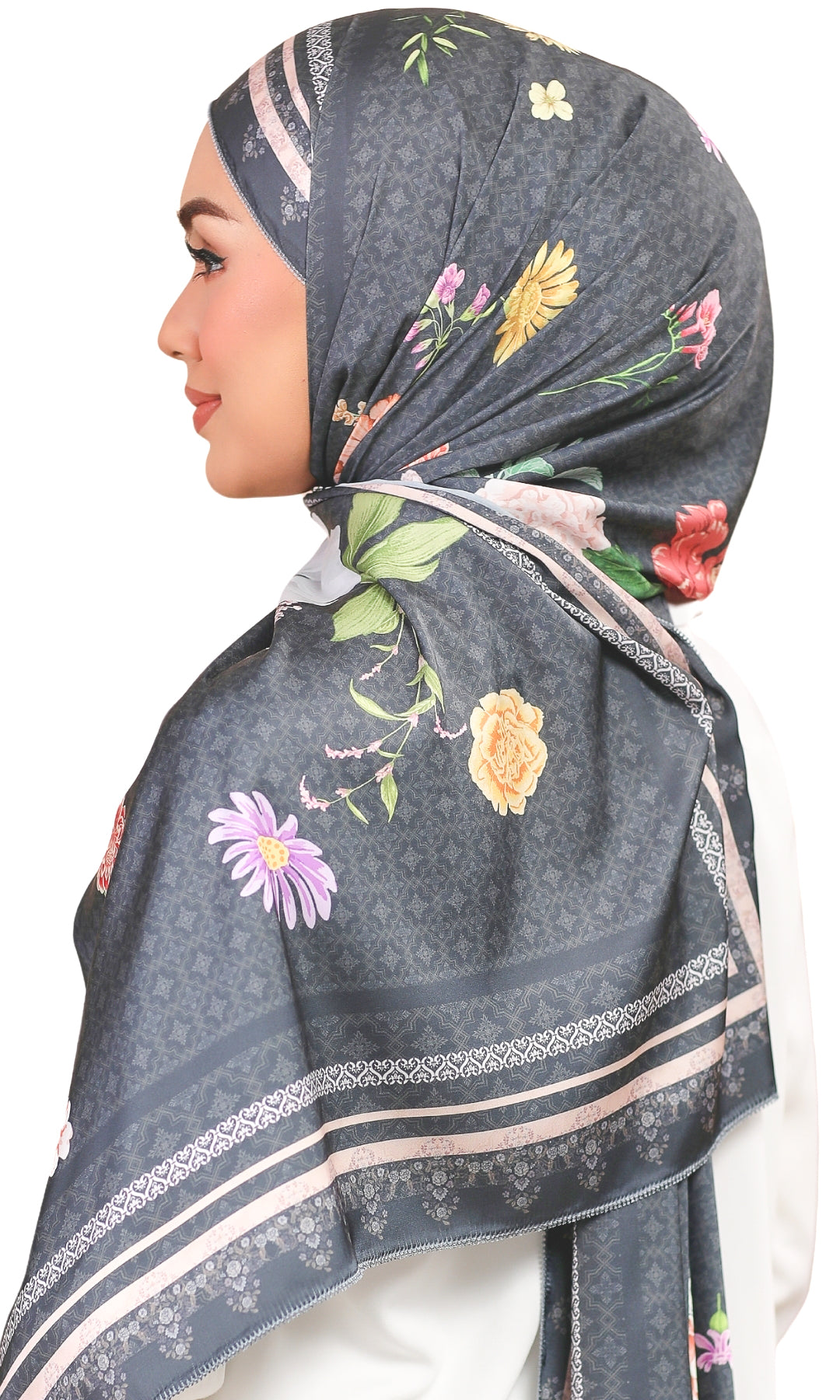 A woman shown in profile wearing a dark gray hijab with a floral print and patterned borders, photographed against a plain white background.
