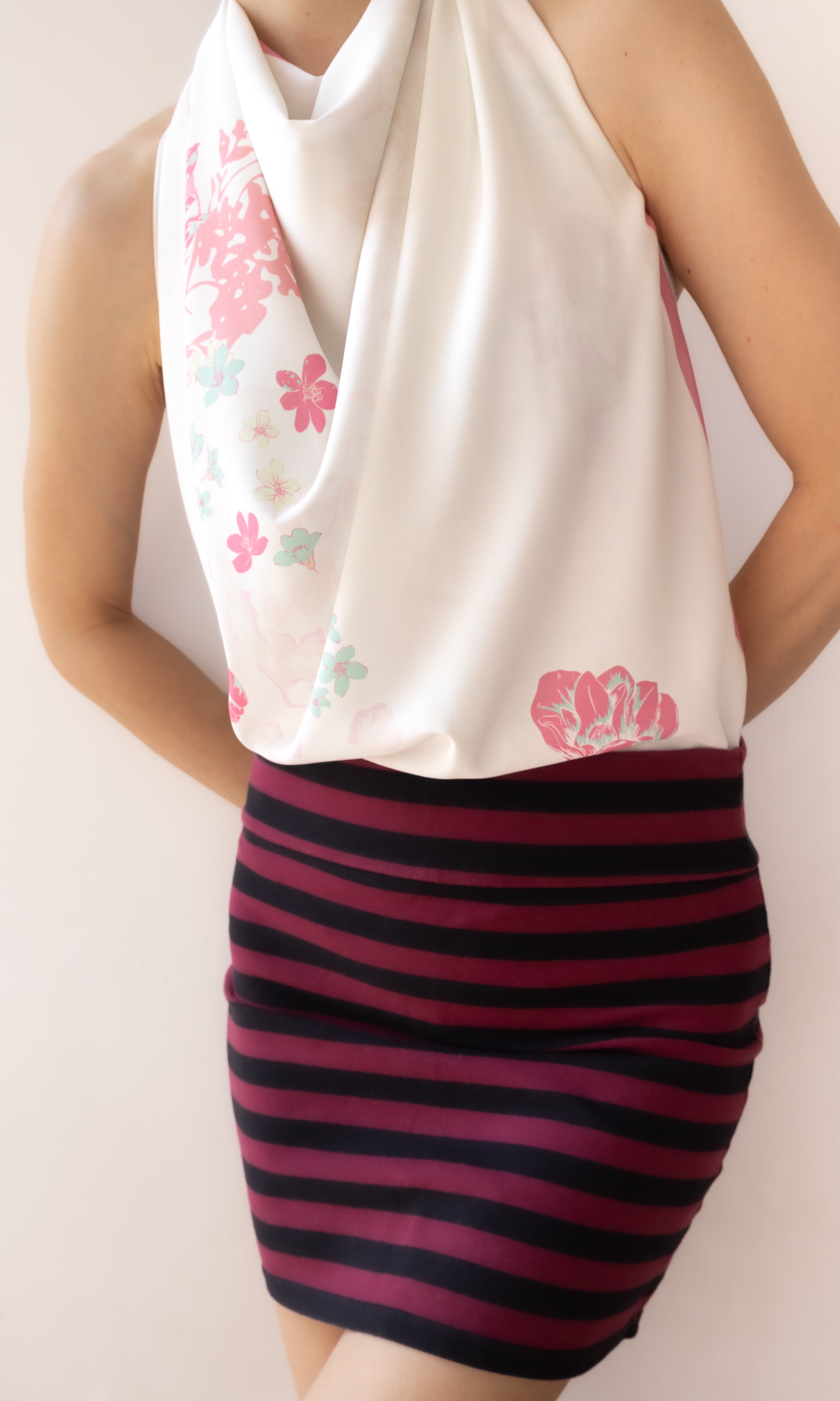 A model wearing a cream halter top with pink and light blue floral prints, paired with a dark pink and navy striped bodycon mini skirt.