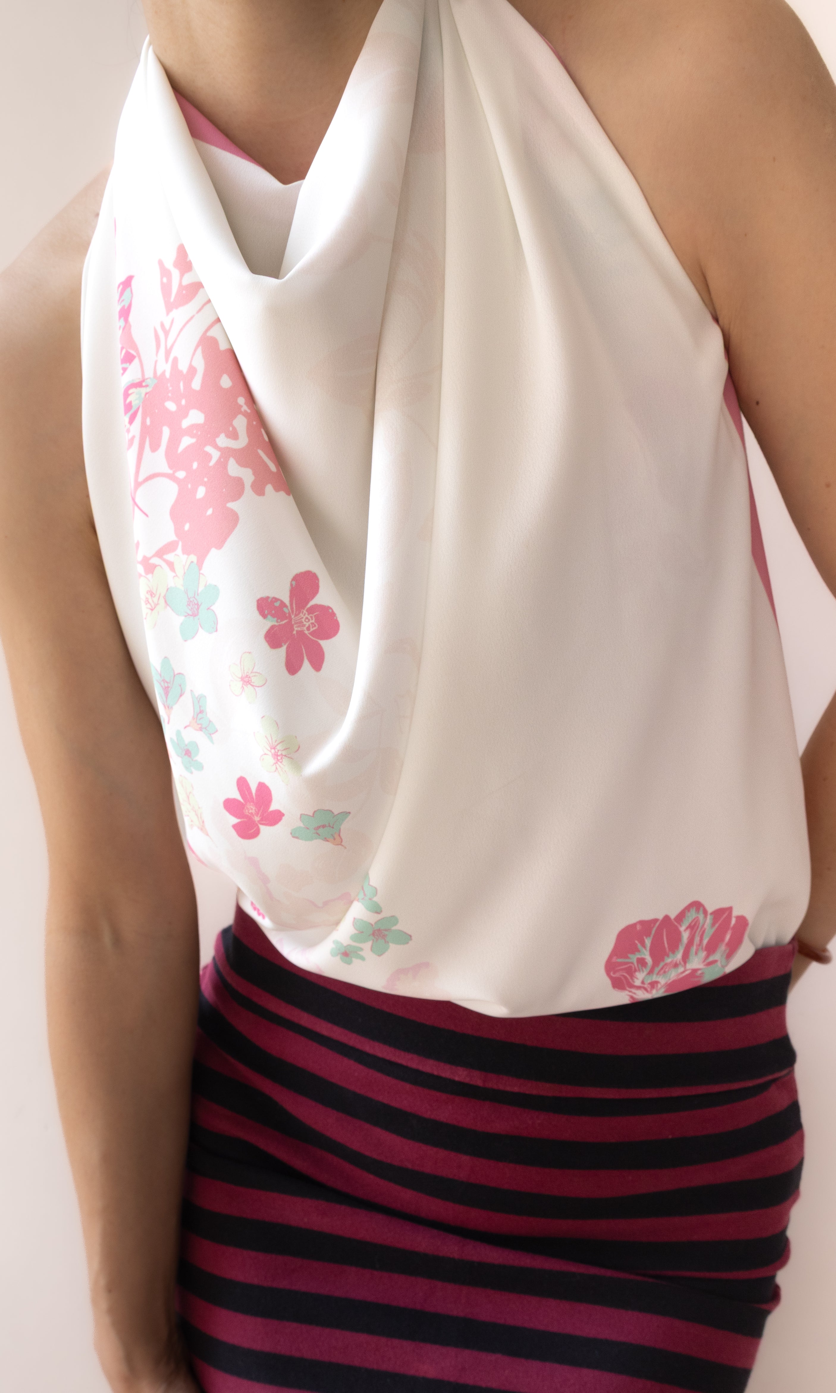 A close-up of a model wearing a white halter-neck top with pink and green floral patterns, paired with a dark pink and navy striped skirt.