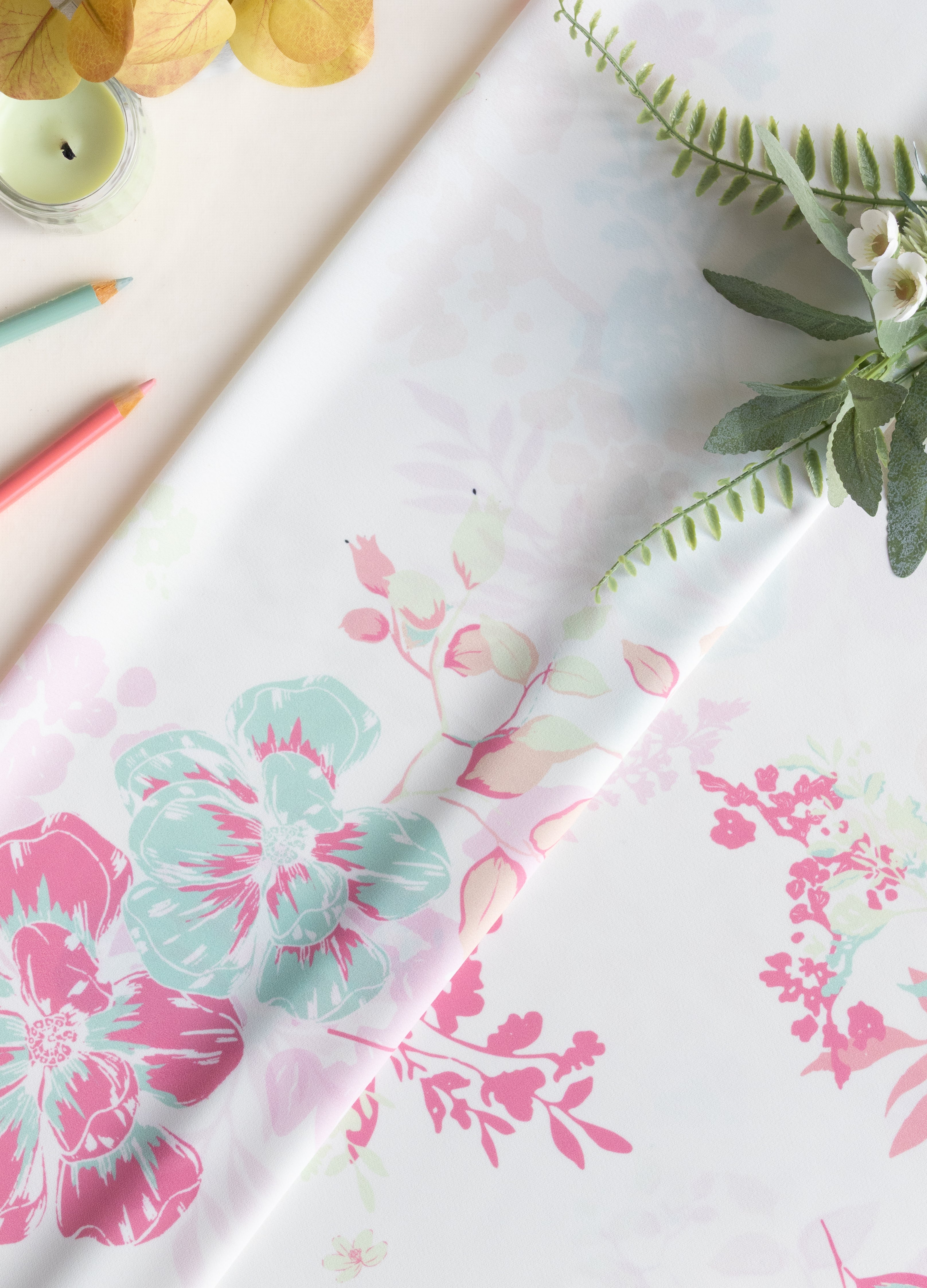 A roll of white wrapping paper with a pink and mint green floral pattern, styled on a light beige surface with decorative greenery and colored pencils.