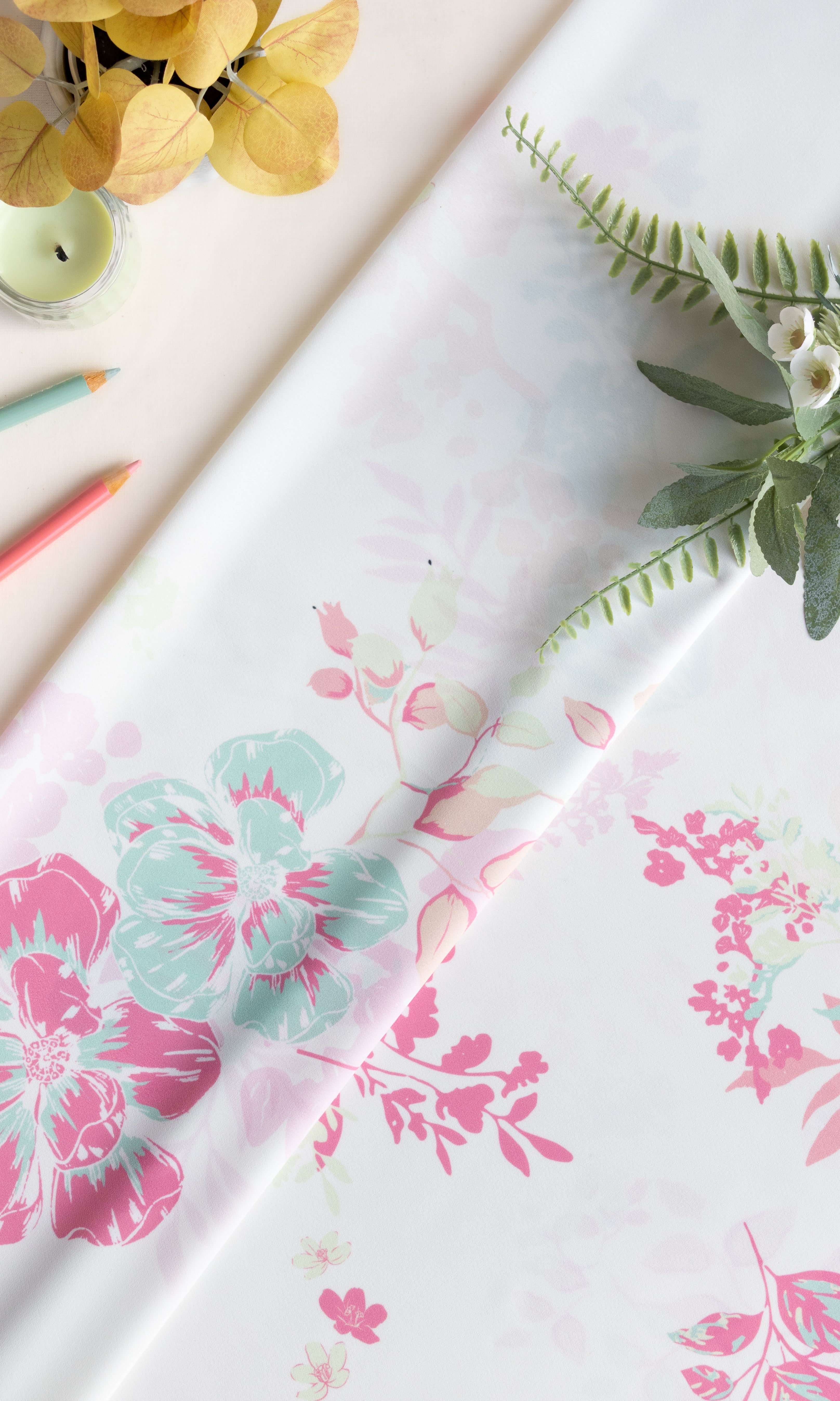 A roll of white wrapping paper with a pink and mint green floral pattern, styled on a light beige surface with decorative greenery and colored pencils.