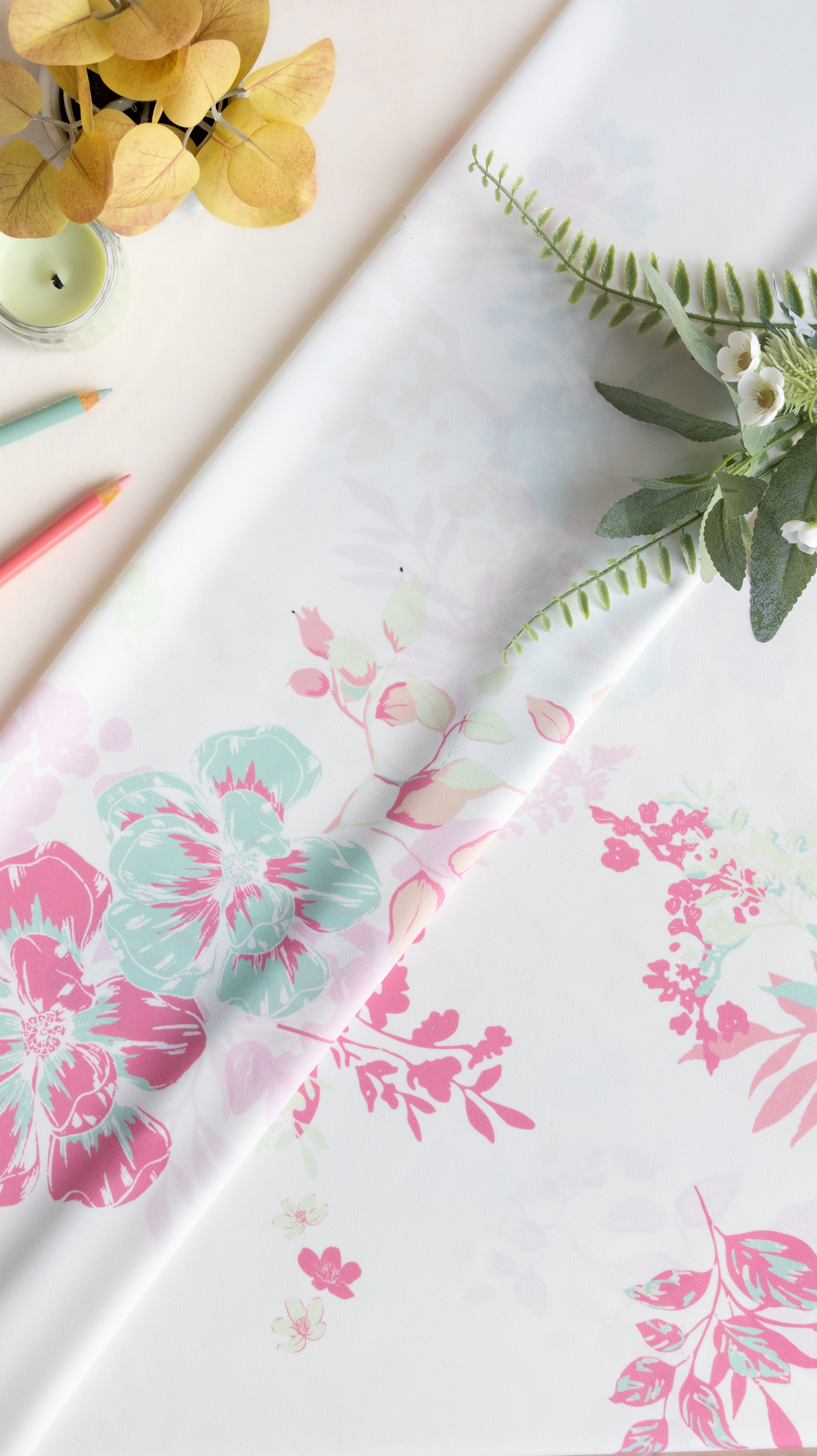 A roll of white wrapping paper with a pink and mint green floral pattern, styled on a light beige surface with decorative greenery and colored pencils.