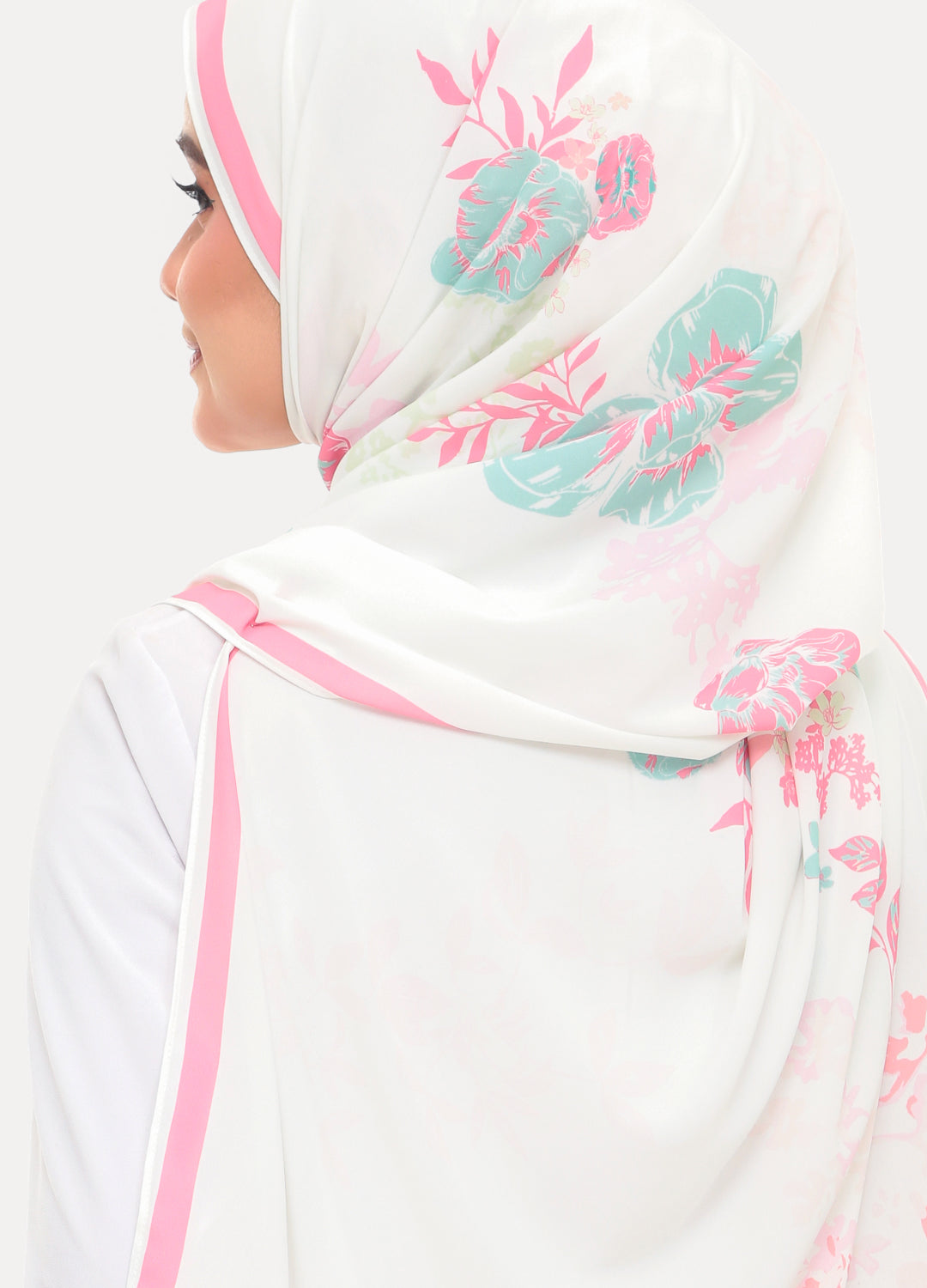 A woman shown from the side wearing a white hijab with pink border trim and teal floral print, against a plain light background.
