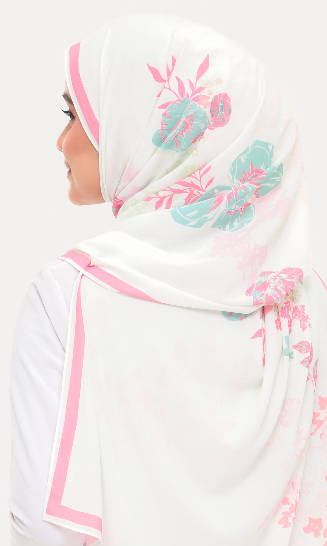 A woman shown from the side wearing a white hijab with pink border trim and teal floral print, against a plain light background.