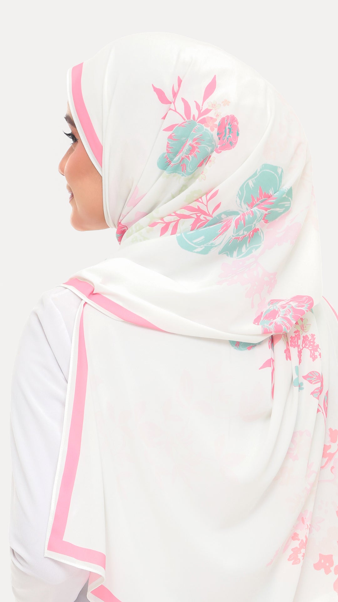 A woman shown from the side wearing a white hijab with pink border trim and teal floral print, against a plain light background.