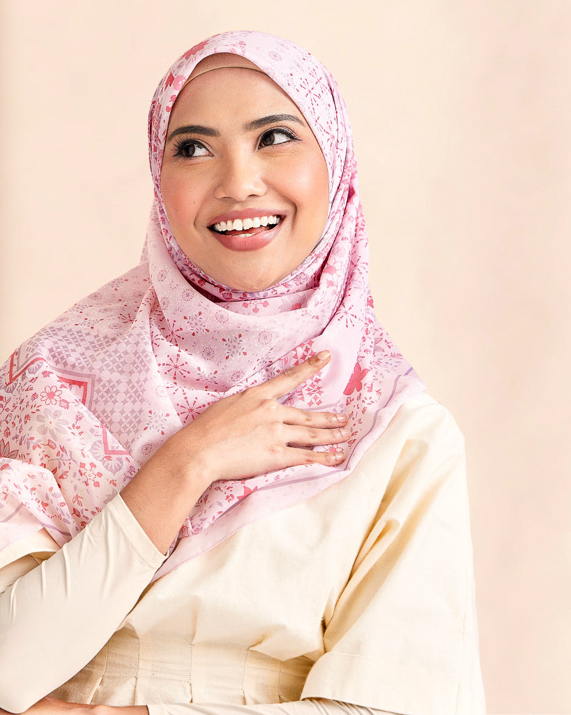 Woman wearing a pink hijab and white top against a beige background