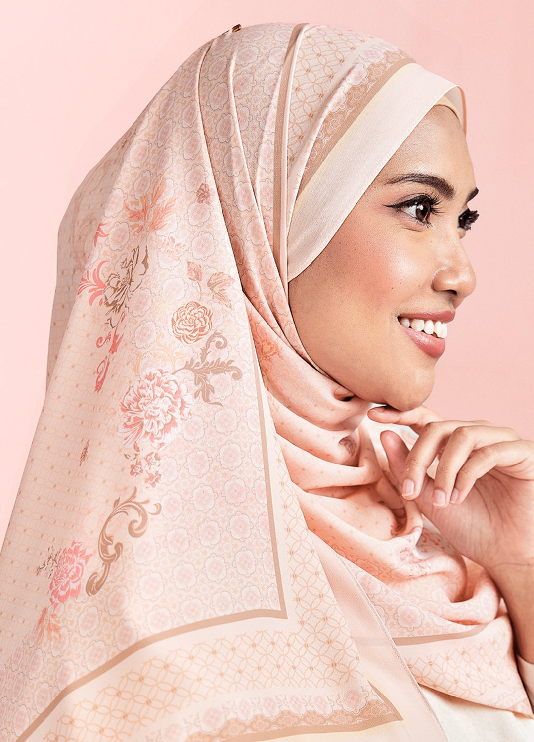 Woman wearing a beige hijab with floral patterns on a pink background