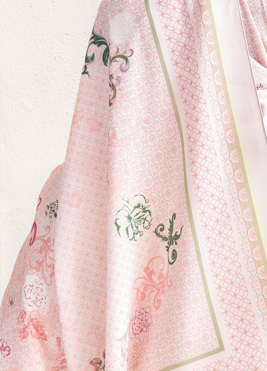 Close-up of a pink fabric with green floral patterns on a light background