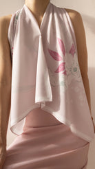 A close-up of a model wearing a light pink halter top and a matching draped scarf with a pink floral print.