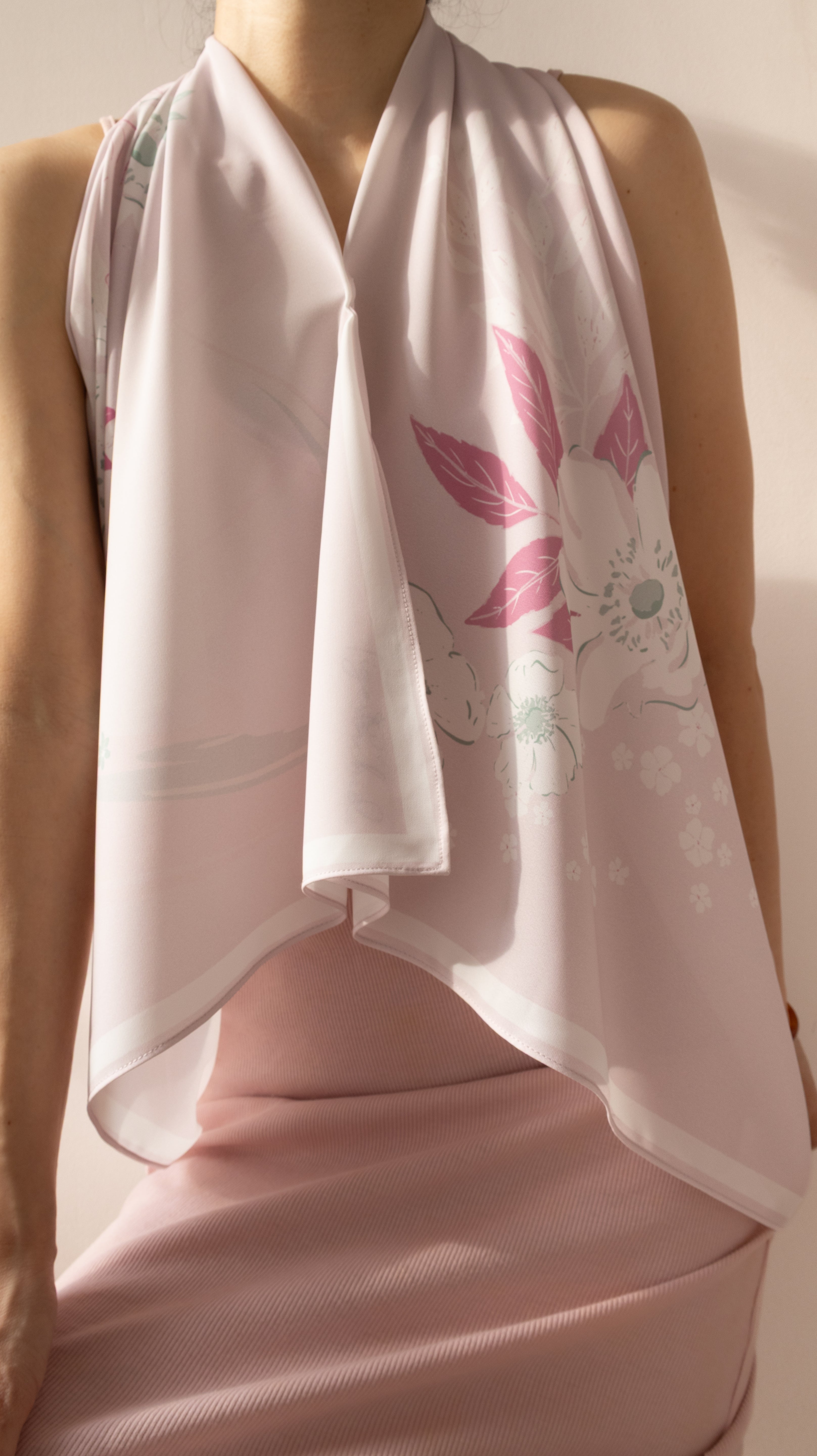 A close-up of a model wearing a light pink halter top and a matching draped scarf with a pink floral print.