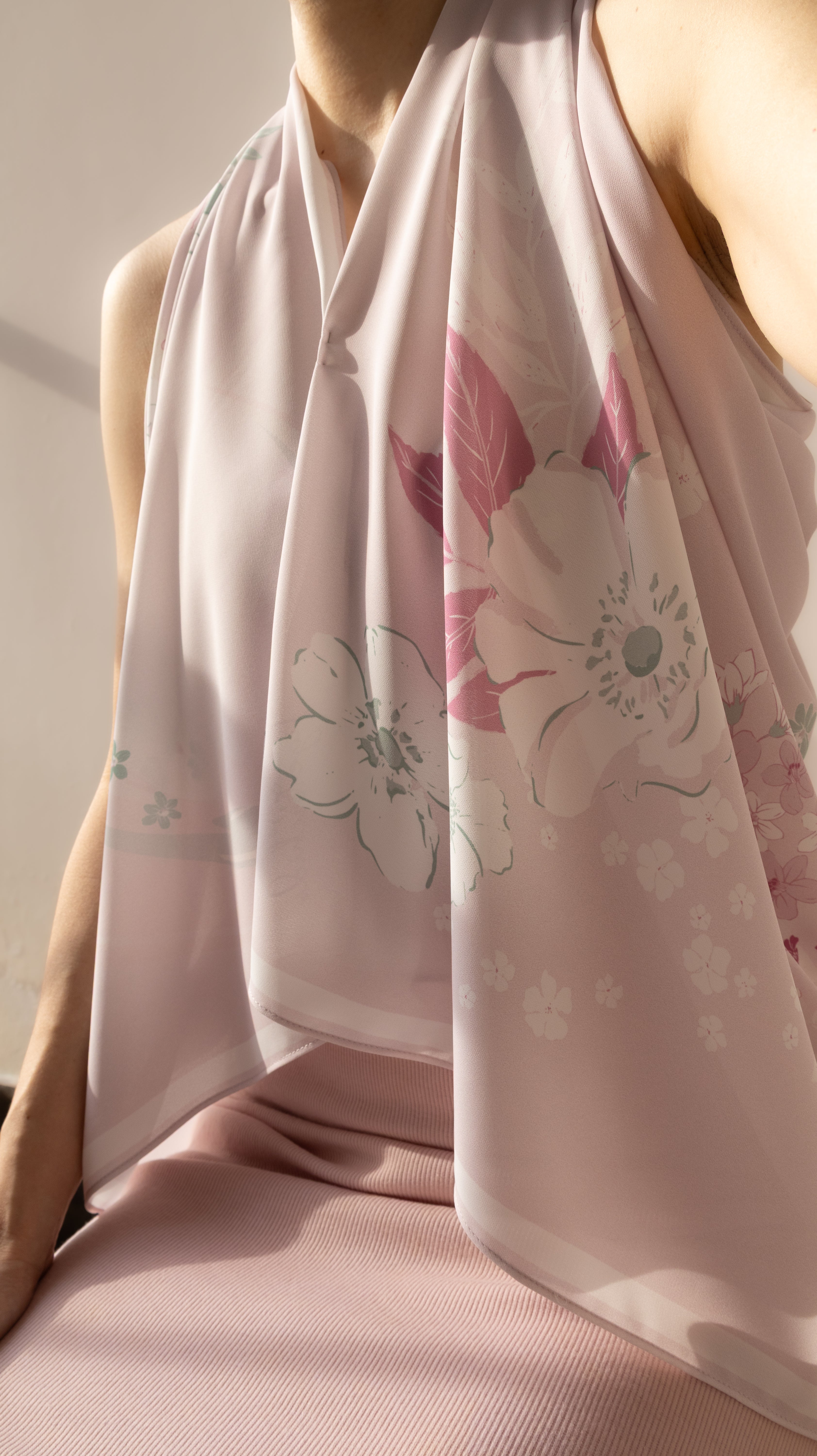 A close-up of a model wearing a light pink halter-neck top and a matching sheer pink scarf with a white and pink floral print.