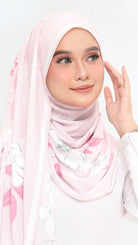 A woman wearing a light pink hijab with a delicate floral print in pink, white, and soft green, paired with a white long-sleeve top against a plain white background.
