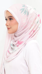 A woman in profile wearing a light pink hijab with a delicate green and pink floral print, paired with a white top against a plain white background.