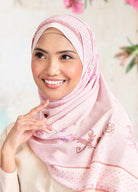 Woman wearing a pink hijab with floral patterns, smiling and posing against a blurred background.
