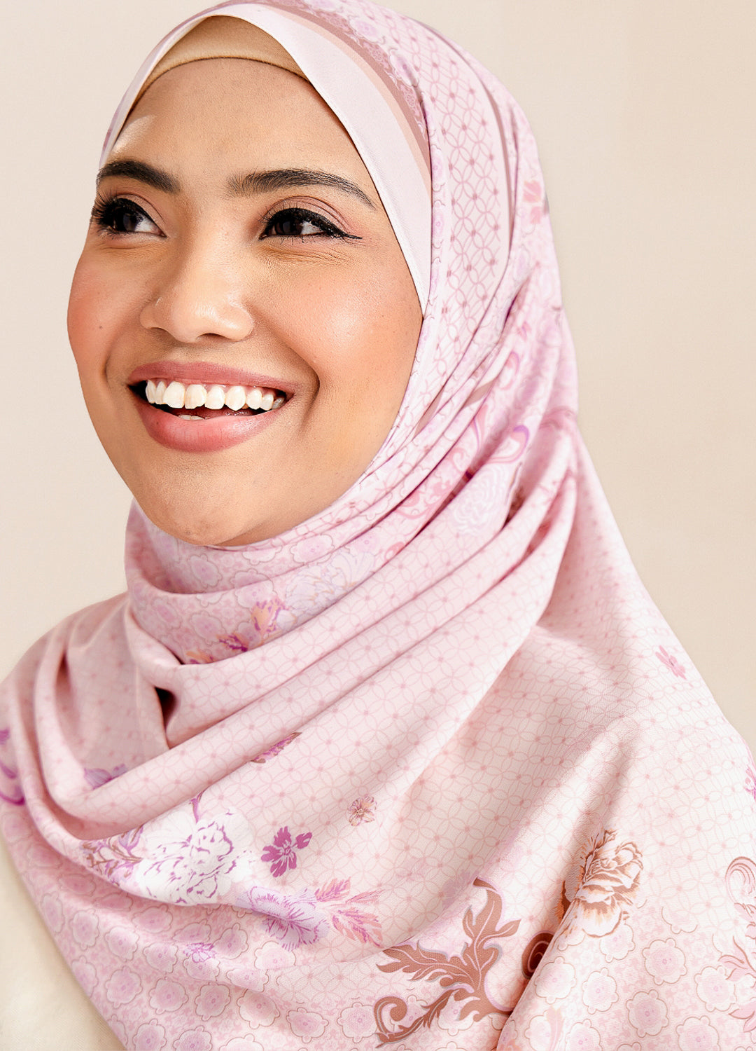 Woman wearing a pink hijab with floral patterns on a beige background