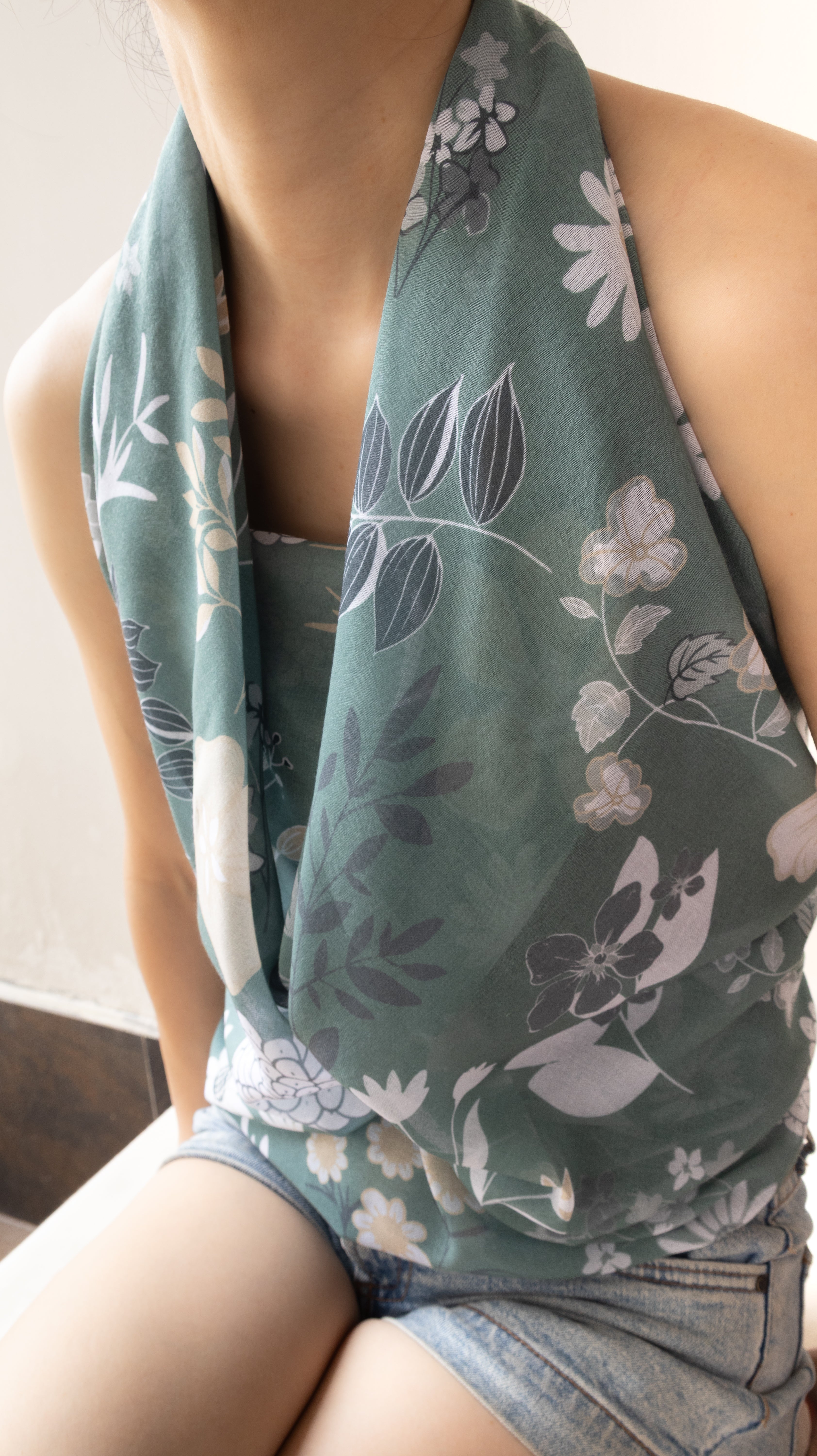 A close-up of a person wearing a sage green halter-style top or scarf with a white and gray floral print, paired with denim shorts.