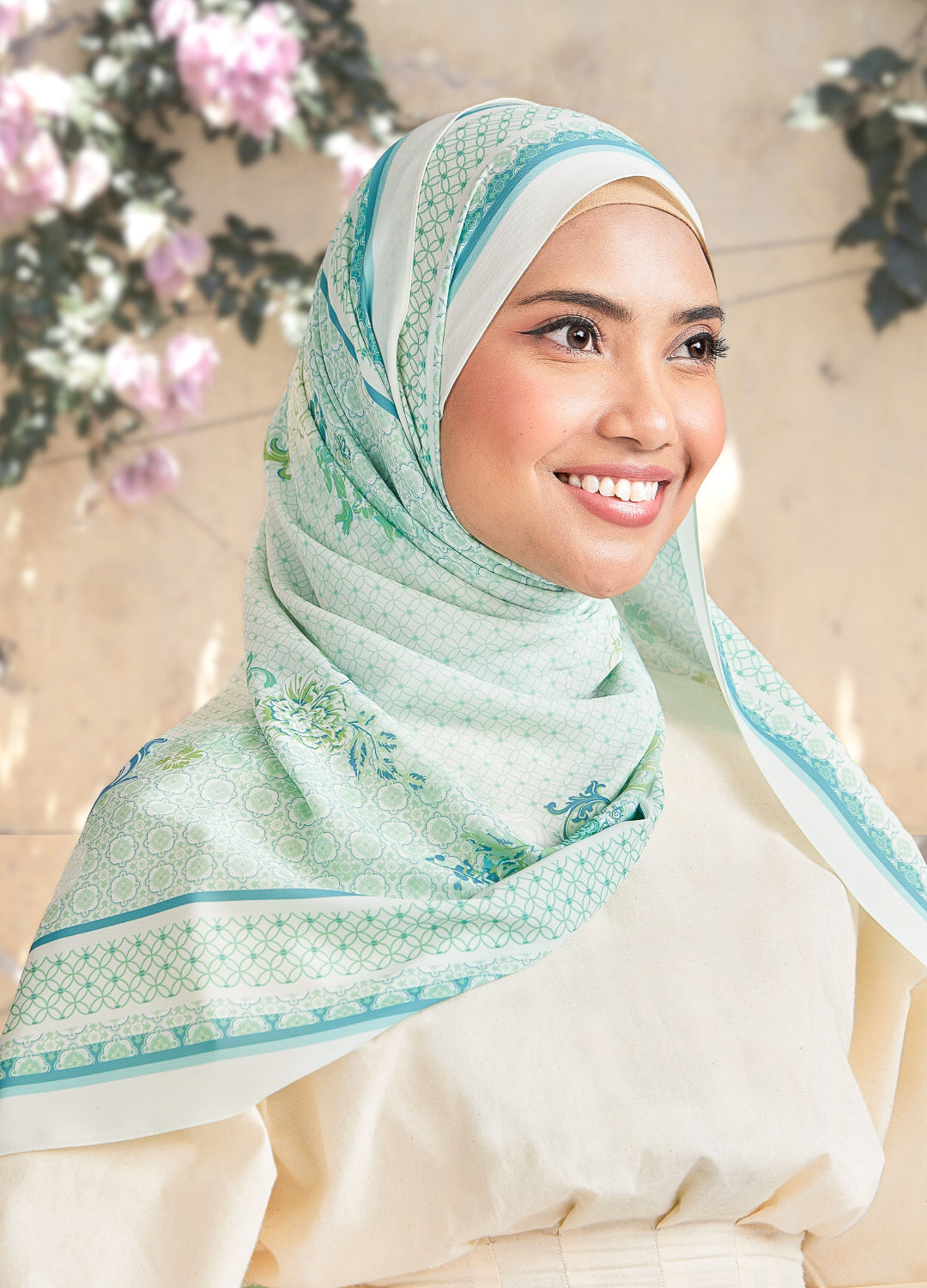 Woman wearing a light green hijab with floral patterns against a blurred floral background