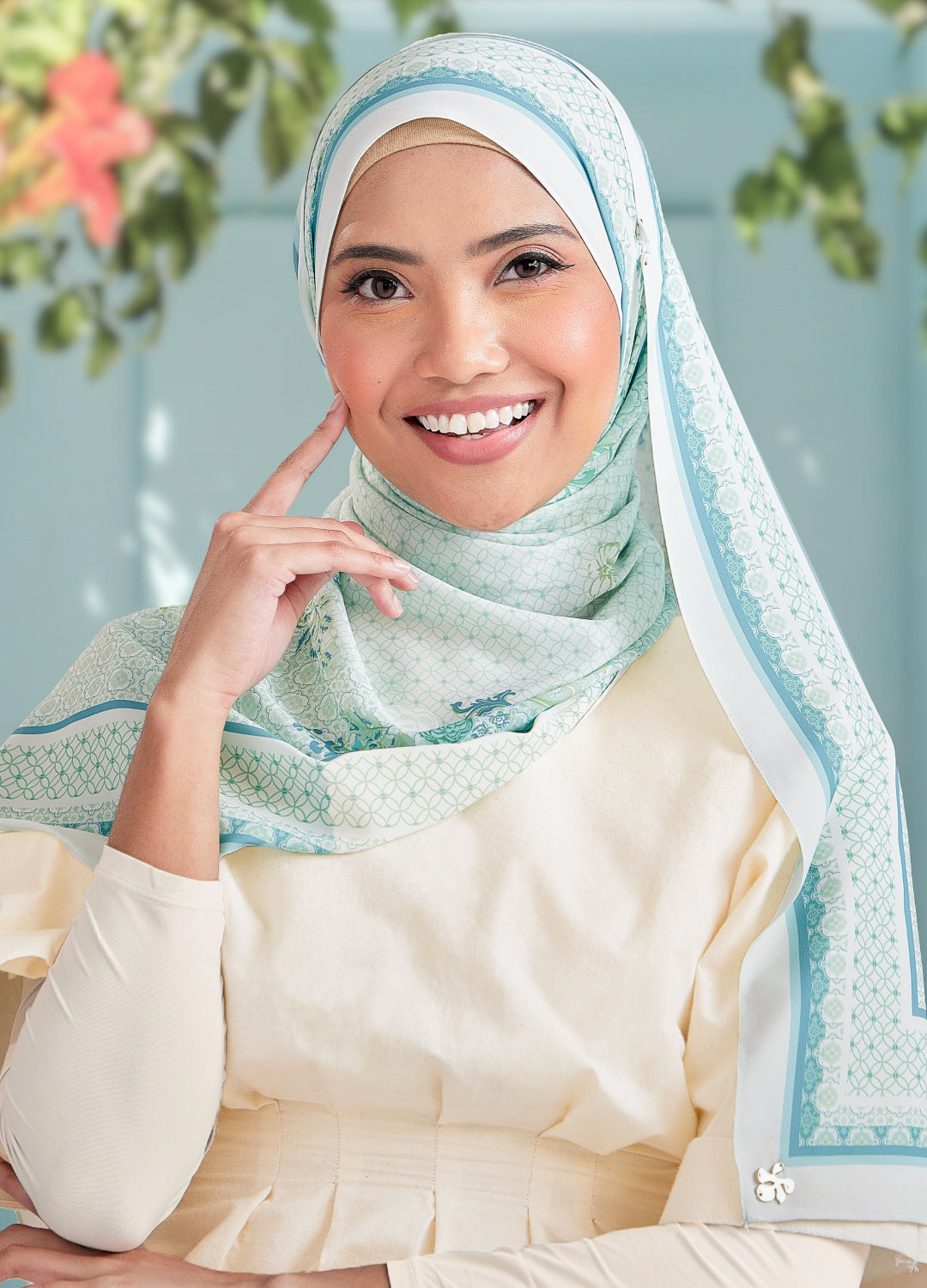 Woman wearing a light blue hijab with floral patterns against a blurred natural background