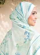 Woman wearing a light green hijab with floral patterns against a neutral background