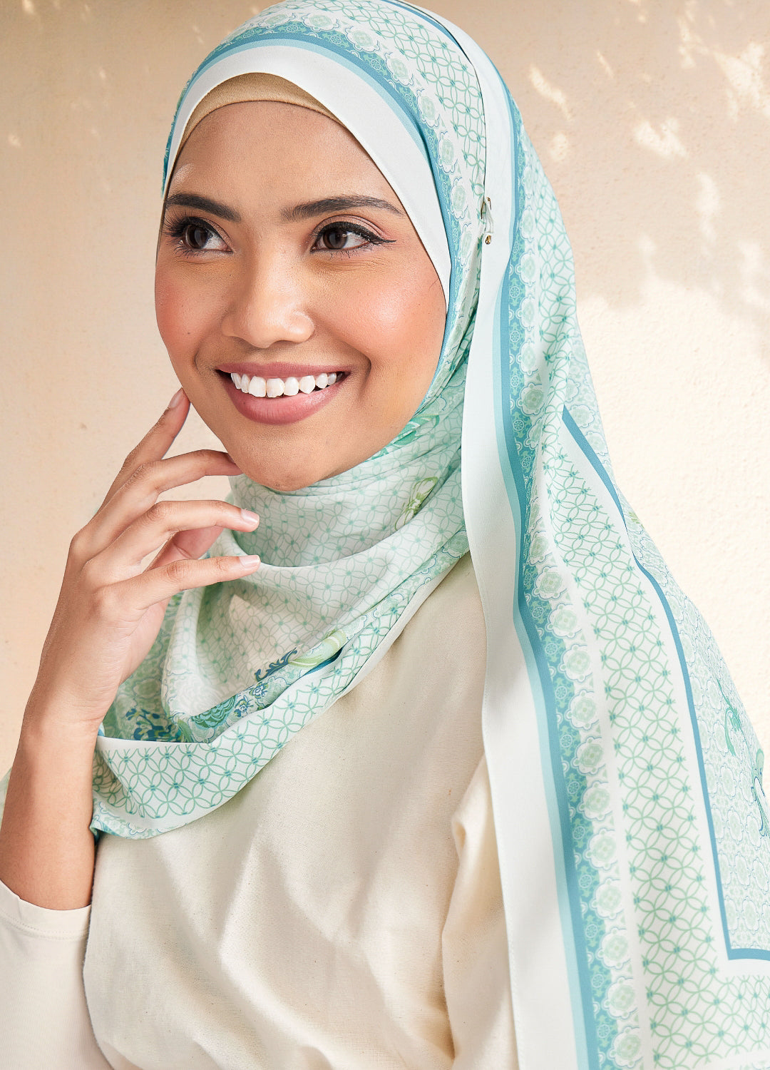 Woman wearing a light blue hijab with a subtle pattern on a beige background