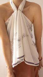 A close-up of a model wearing a cream-colored halter top with a delicate gray floral print and purple striped trim at the hem.