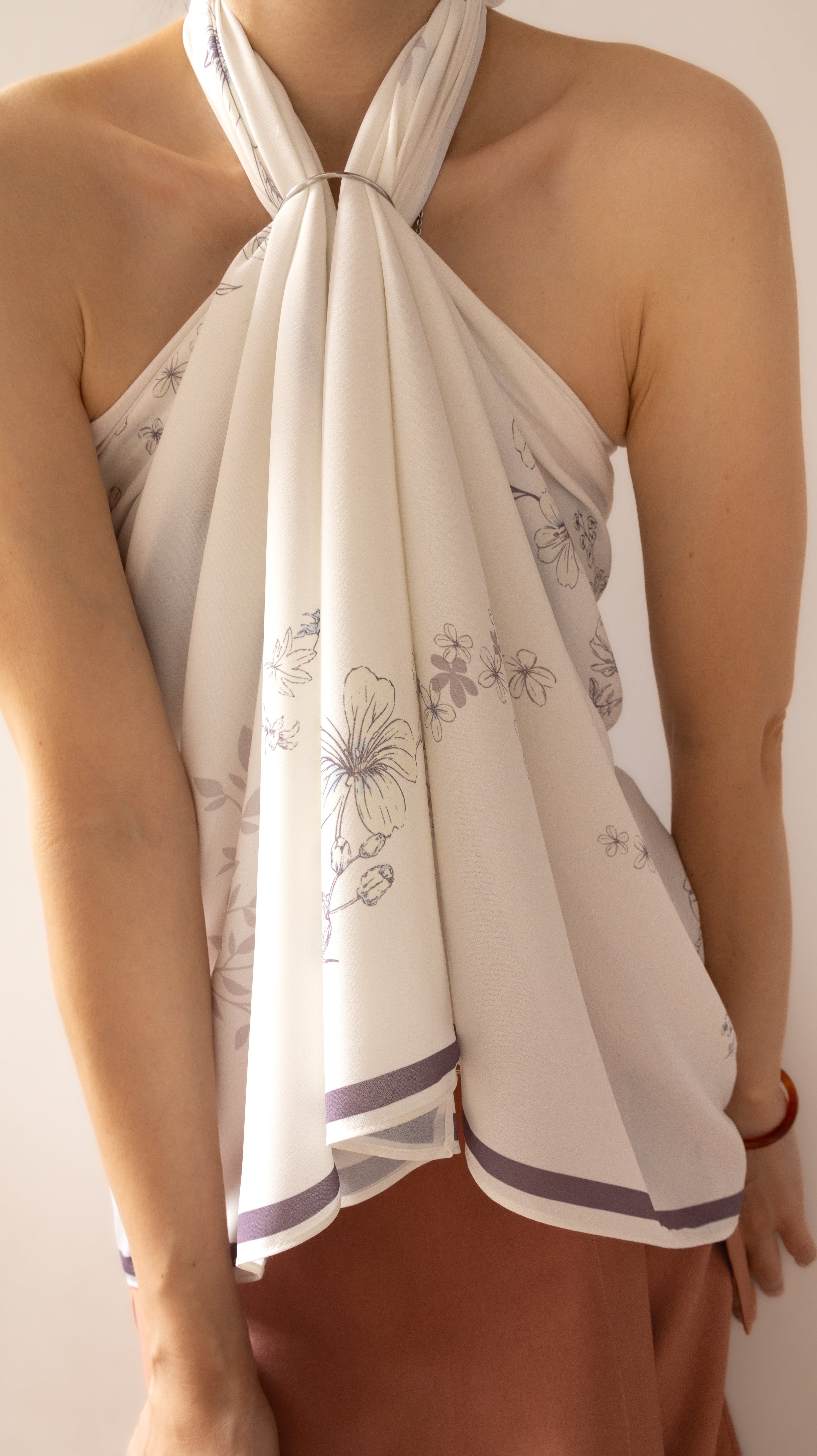 A close-up of a model wearing a cream-colored halter top with a delicate gray floral print and purple striped trim at the hem.