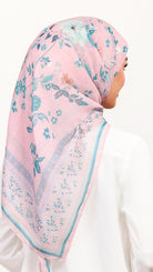 A woman shown from the back wearing a light pink hijab with a blue and green floral pattern and a matching border, paired with a white top against a plain white background.