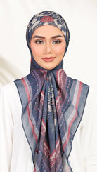 A woman wearing a patterned hijab in navy blue, dusty pink, and beige, paired with a white top against a soft white background.