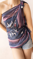 A woman wearing a draped, one-shoulder wrap top made from a navy blue patterned scarf with red and white accents, paired with denim shorts.
