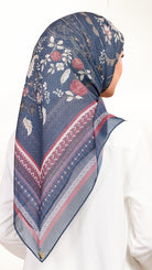 A woman shown from the back wearing a navy blue patterned hijab with floral motifs and geometric borders, paired with a white top against a plain white background.