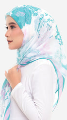 A woman in profile wearing a white hijab with a light blue and pink floral pattern, paired with a white long-sleeve top, against a plain white background.
