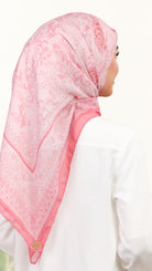 A woman shown from the back wearing a light pink patterned hijab and a white long-sleeve top against a plain white background.