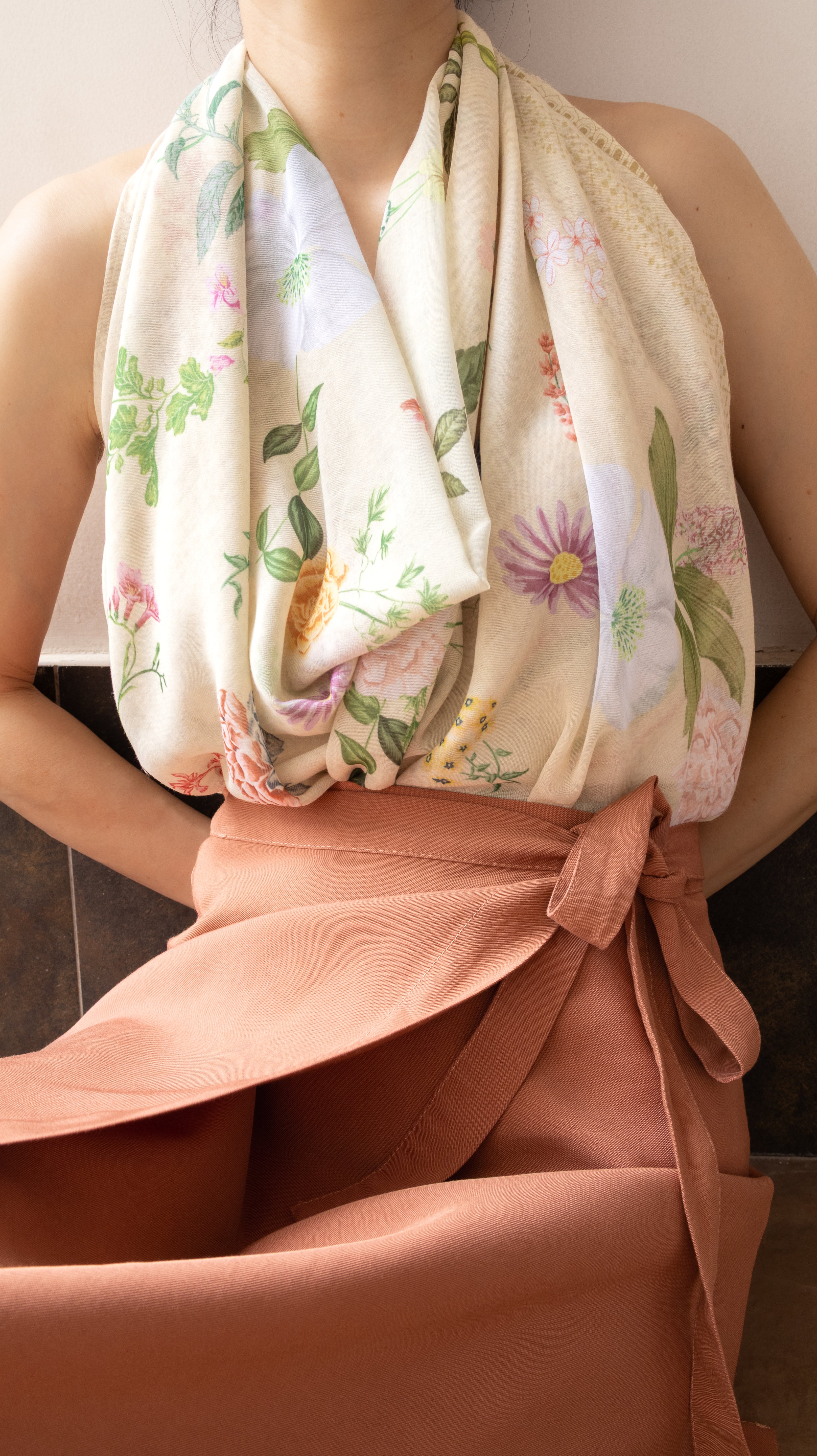 A close-up of a person wearing a cream-colored floral halter top or dress with a matching peach wrap skirt tied at the waist.