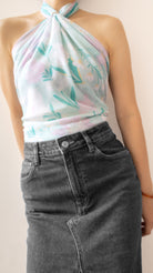 A close-up of a person wearing a pastel halter top with a light blue, pink, and green floral print, paired with a dark gray denim skirt.