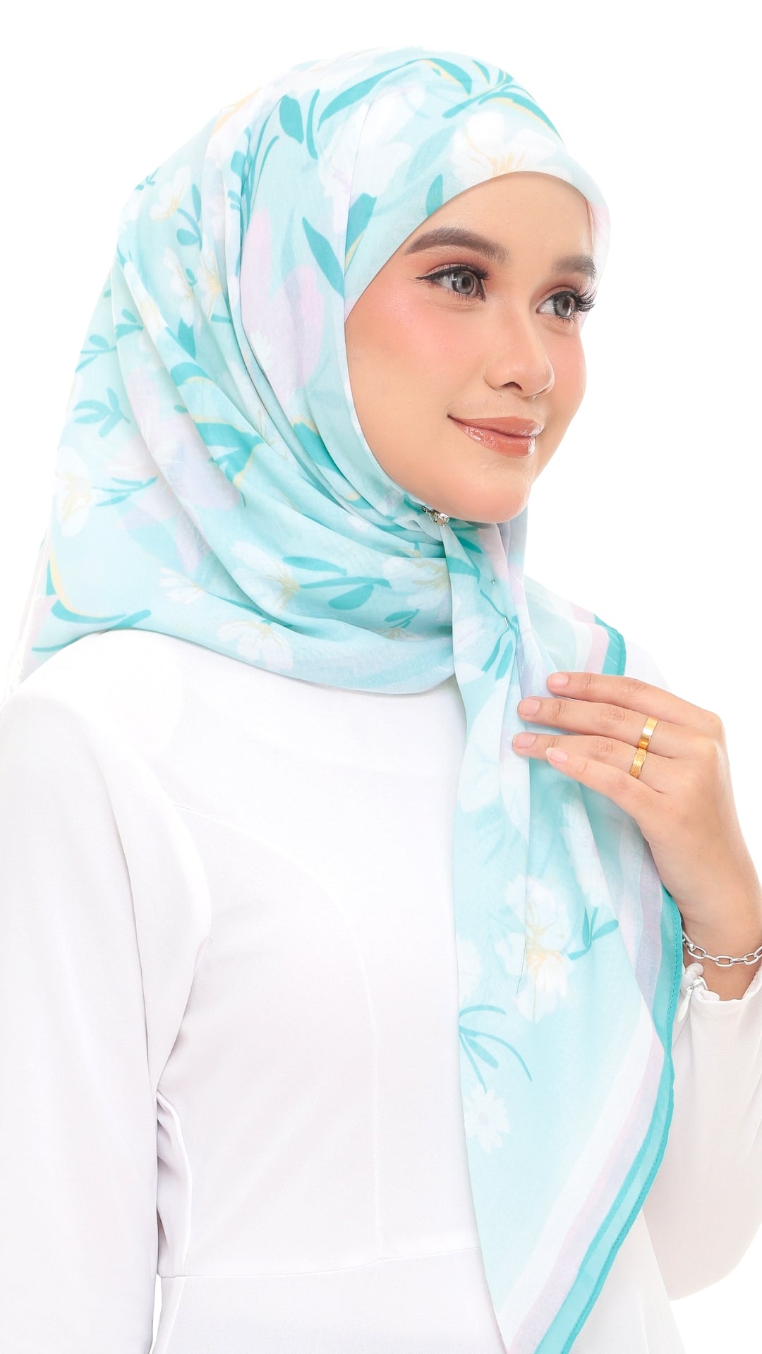 A woman wearing a light blue and white floral print hijab, paired with a white long-sleeve top, photographed against a solid white background.