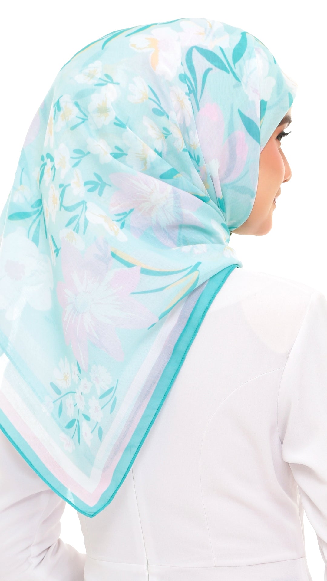 A woman wearing a light aqua hijab with a pastel floral print in pink, white, and green, paired with a white top against a plain white background.