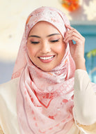 Woman wearing a pink hijab with floral patterns, smiling outdoors.