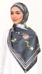 A woman wearing a dark gray patterned hijab with colorful floral prints and beige borders, styled over a white top against a plain white background.