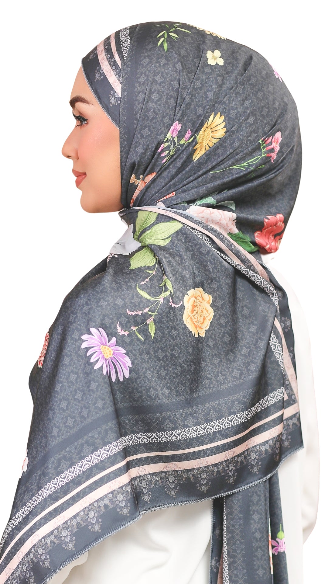 A woman shown in profile wearing a dark gray hijab with a floral print and patterned borders, photographed against a plain white background.
