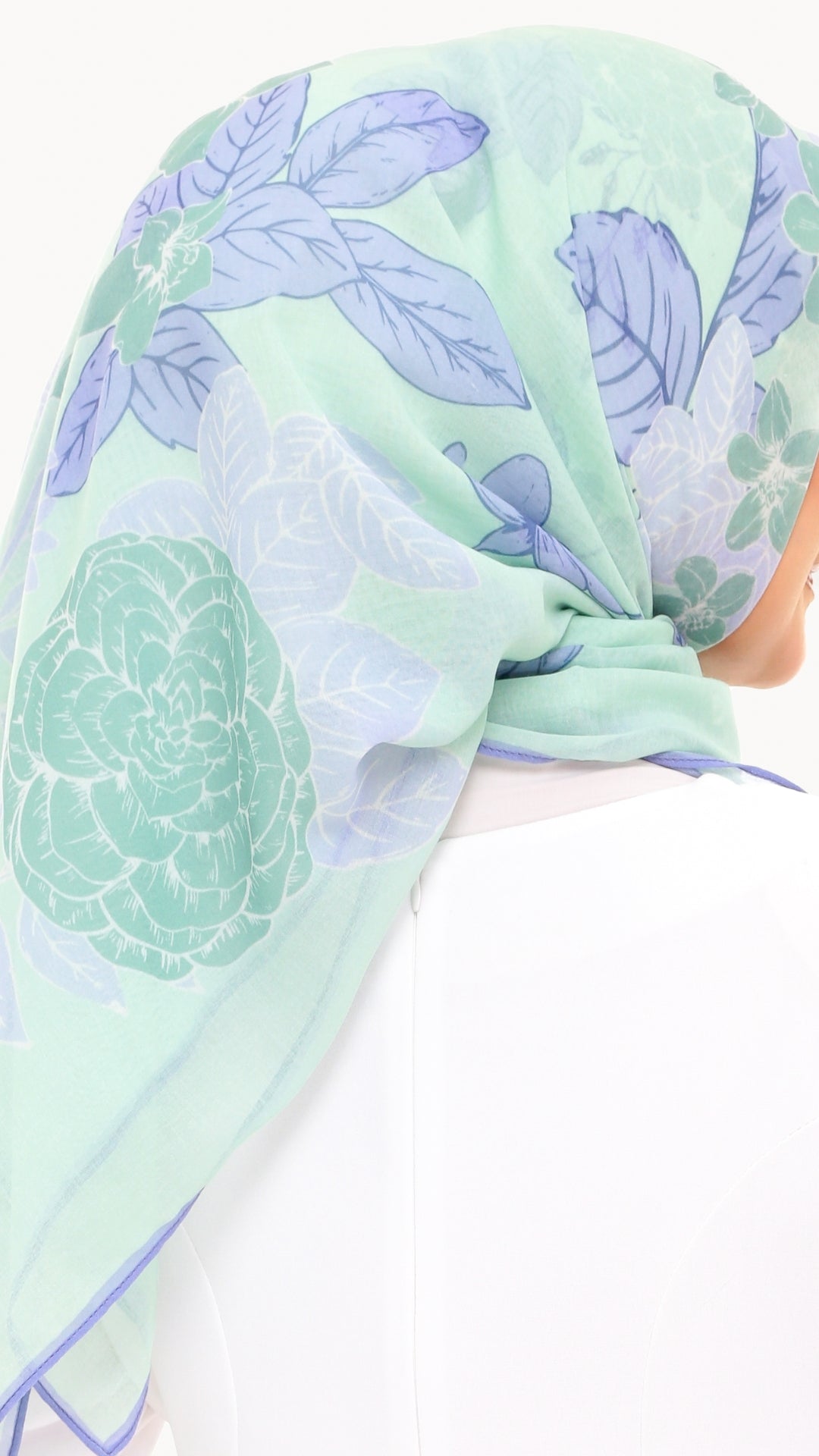 A mint green and light purple floral print headscarf tied under the chin, shown on a mannequin head against a white background.