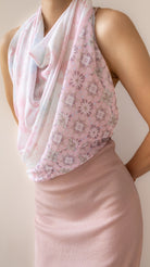 A close-up of a model wearing a draped halter-style scarf with a light pink and white floral pattern, paired with a solid pale pink top.