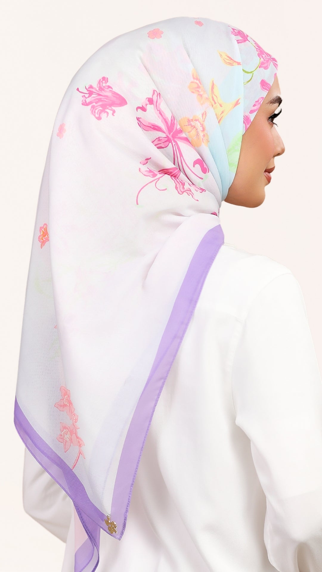 A woman shown in profile wearing a white hijab with pastel pink floral prints and a lavender border, against a plain light background.
