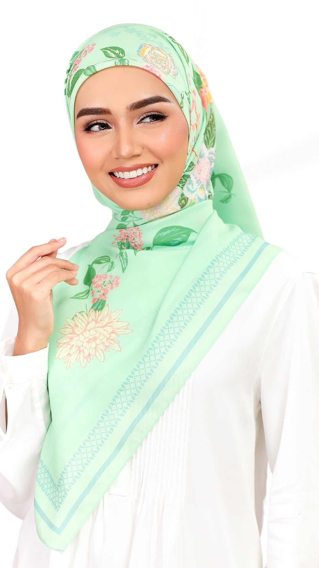 A woman wearing a mint green floral hijab and a white top, photographed against a plain white background.