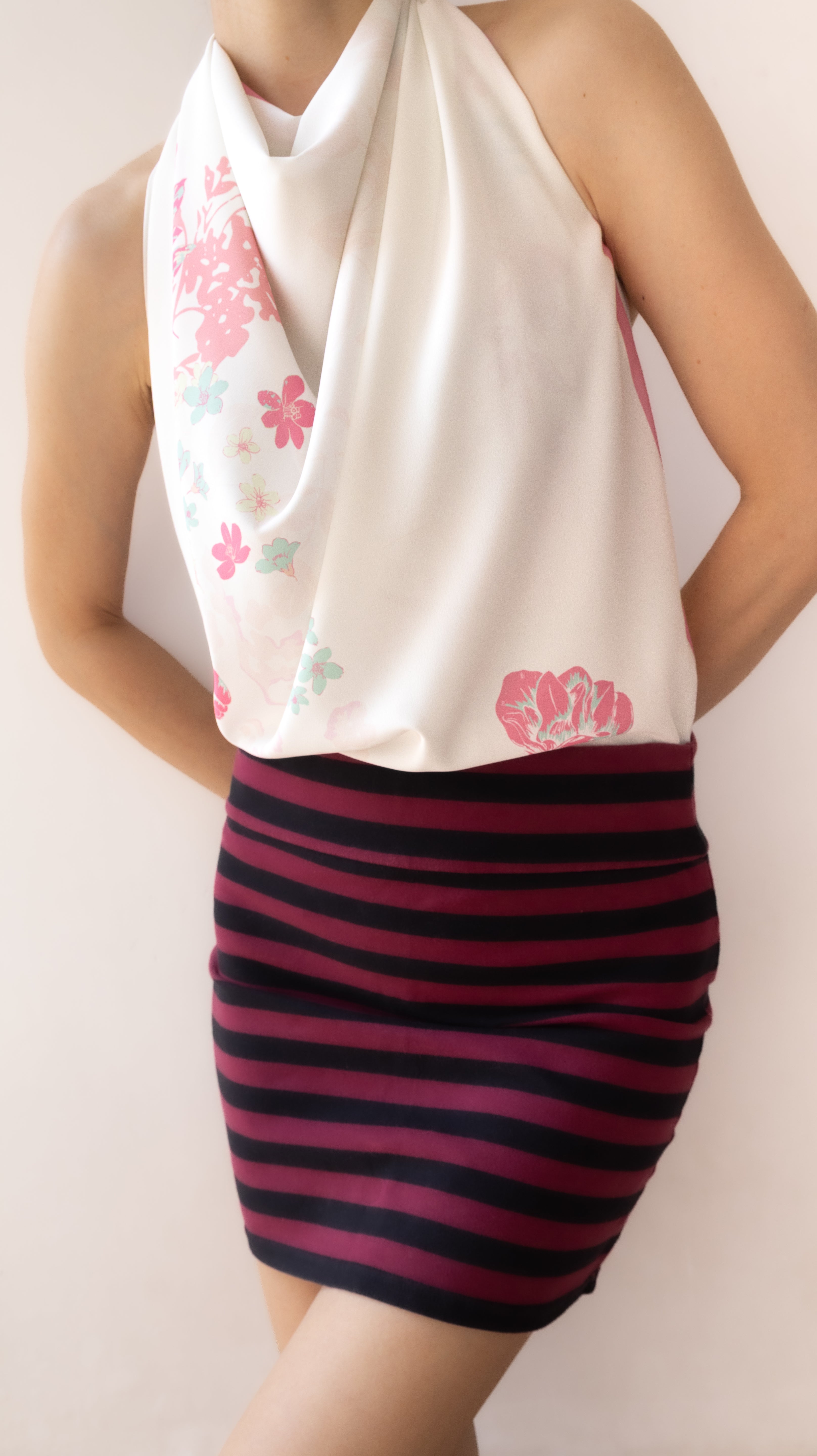 A model wearing a cream halter top with pink and light blue floral prints, paired with a dark pink and navy striped bodycon mini skirt.