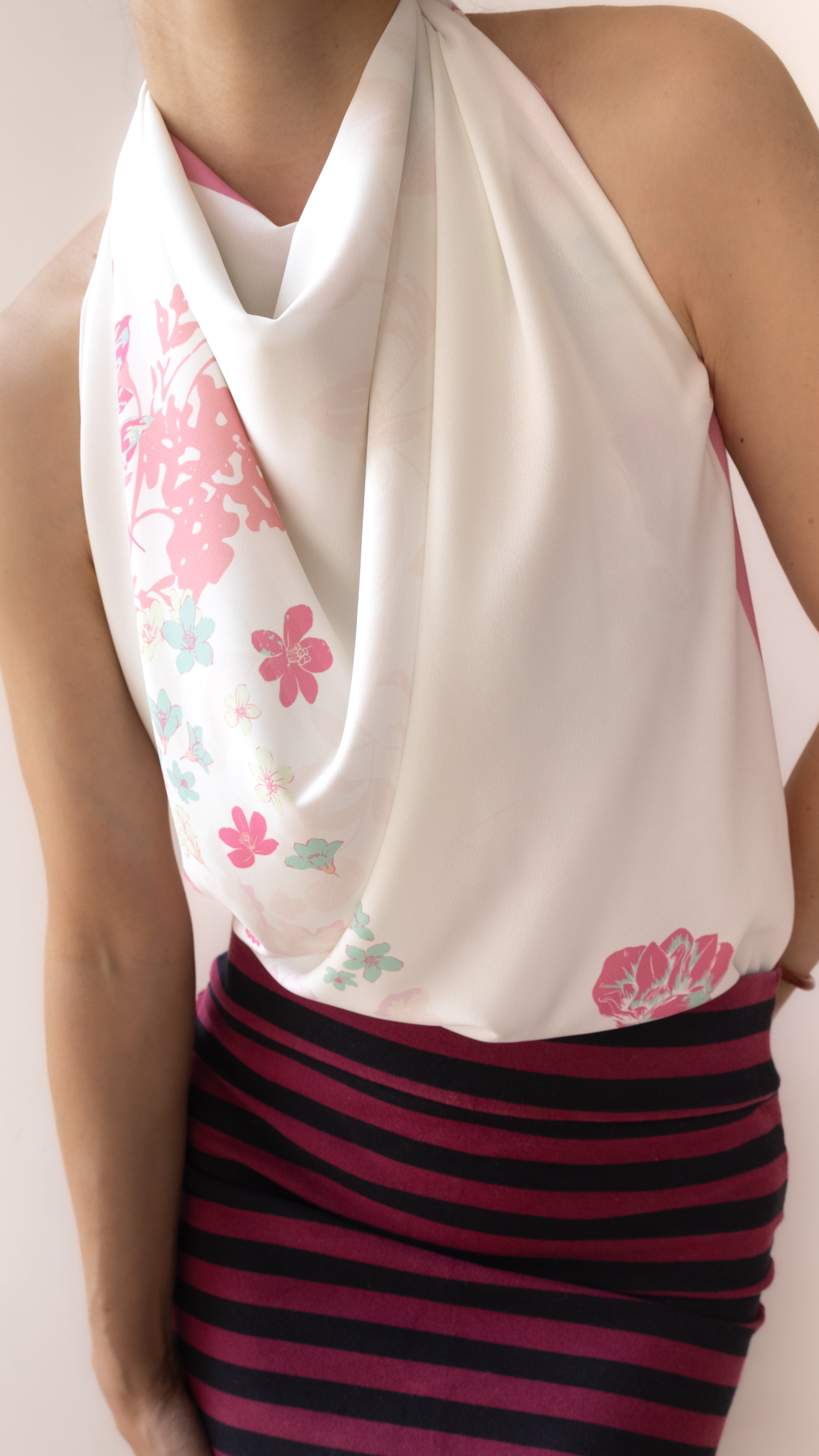 A close-up of a model wearing a white halter-neck top with pink and green floral patterns, paired with a dark pink and navy striped skirt.